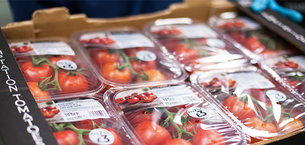 Una caja de cartón lleva varios paquetes de tomates de alta sellado con etiquetas impresas